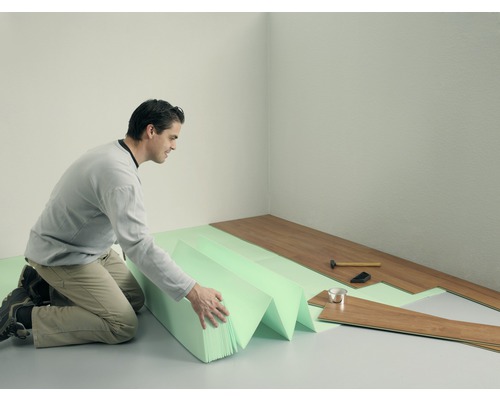 En man lägger laminatgolv med stegljudsisolering i ett rum.