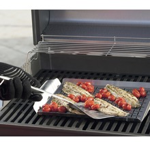 Fisk och tomater tillagas på en grillplatta med en grillspade på en grill.