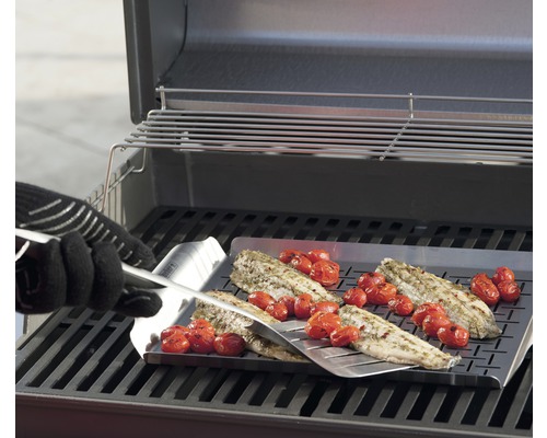 Fisk och tomater tillagas på en grillplatta med en grillspade på en grill.