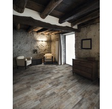 Rustikt rum med takbjälkar i trä, stenväggar, trägolv, byrå och fåtöljer.