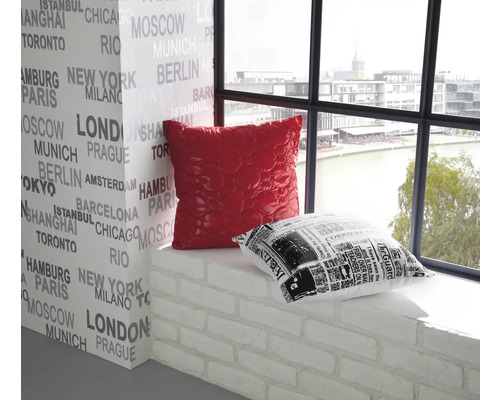 Dekorativ interiör med en röd och en svartvit kudde på en fönsterbräda framför en vägg tryckt med stadsnamn