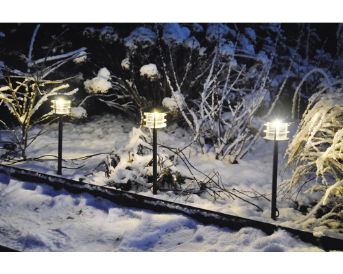 Scen med tre trädgårdslampor i ett snöigt landskap