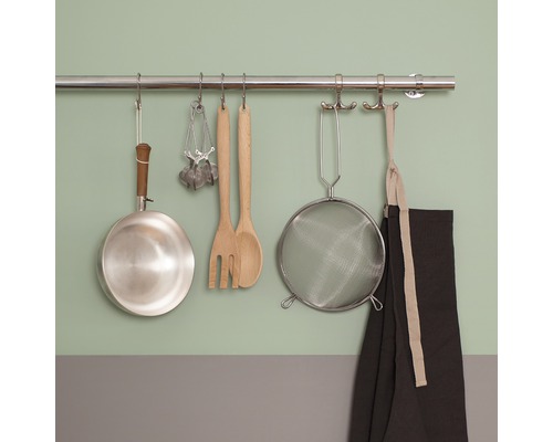 Köksredskap hänger på en stång: stekpanna, måttskedar, salladsbestick, sil och förkläde.