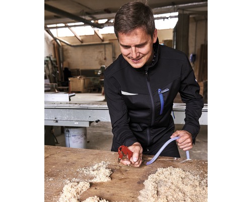 En man i arbetskläder använder en blåsspistol på ett bord med träflis.