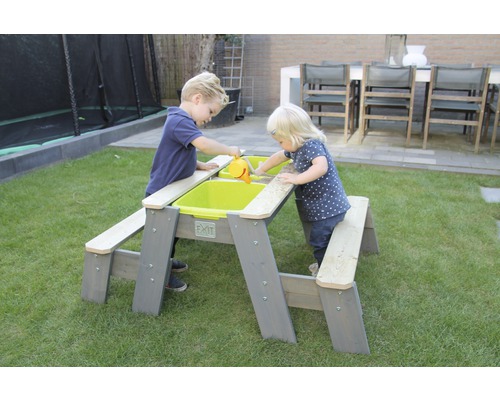 Två barn leker vid ett EXIT picknickbord med sand och vatten i trädgården.