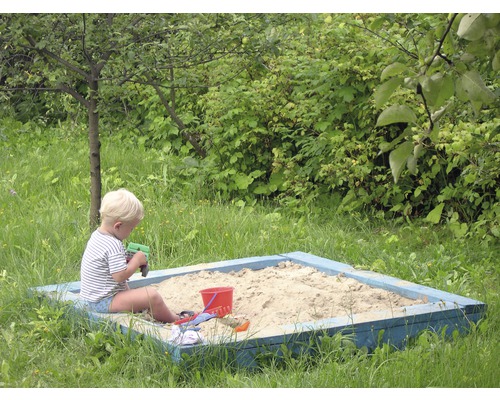 Pojke leker i sandlådan med sandleksaker i trädgården.