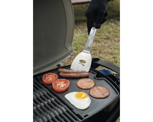 Grill med korv, tomater, bacon och stekt ägg samt en person med stekspade