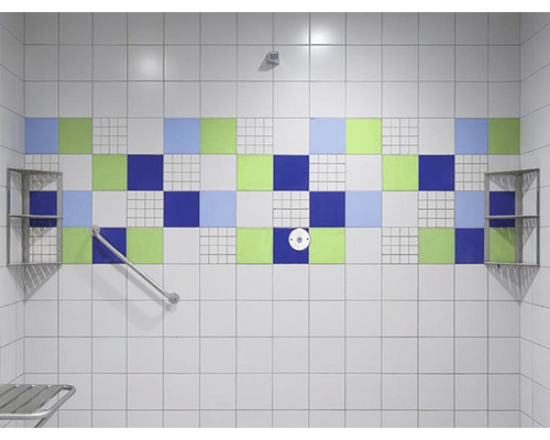 Badrum med vita plattor, blå, gröna och vita accentplattor, ledstång och hyllor