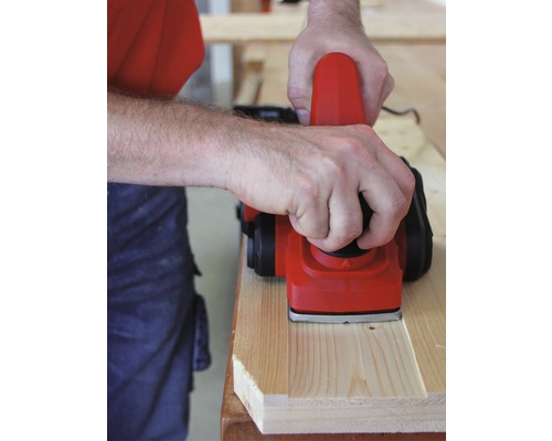 En person hyvlar en träplanka med en elektrisk hyvel.