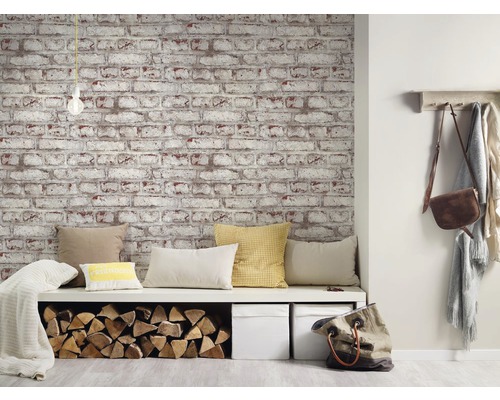 Vardagsrum med tapet i tegelstenslook, sittbänk med kuddar och vedförvaring.