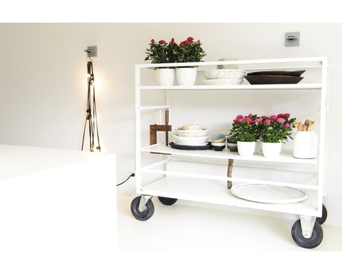 En vit rullvagn med blomkrukor, skålar och dekorativa föremål i ett ljust rum.