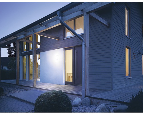 Belyst bostadshus med träfasad och träterrass i skymningen