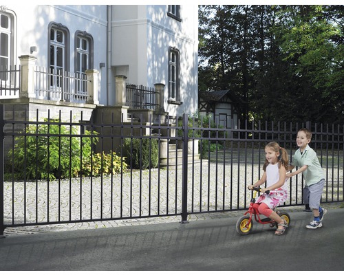Svart metallstaket framför en byggnad med lekande barn