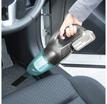 Person som dammsuger fotutrymmet i en bil med en sladdlös handdammsugare från Makita.