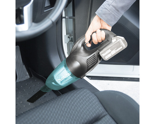 Person som dammsuger fotutrymmet i en bil med en sladdlös handdammsugare från Makita.