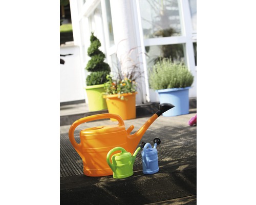 Tre vattenkannor i olika storlekar framför planterade blomkrukor