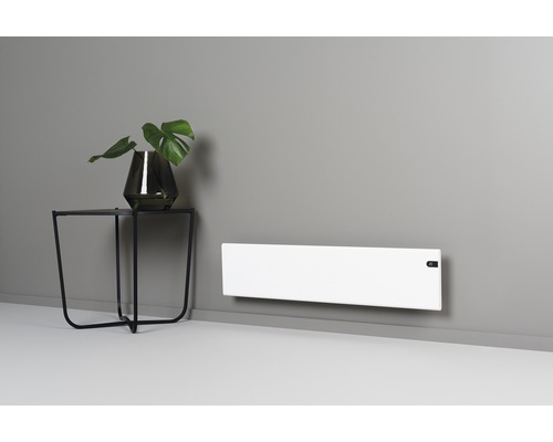 Miljöbild med ett vitt element på väggen och ett sidobord med en växt