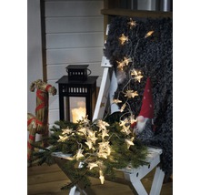 Dekorativ scen med stjärneljusslinga, lykta och tomte på en pall.