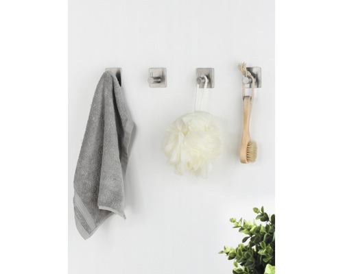 Tre väggkrokar med handduk, duschboll och borste på en vägg