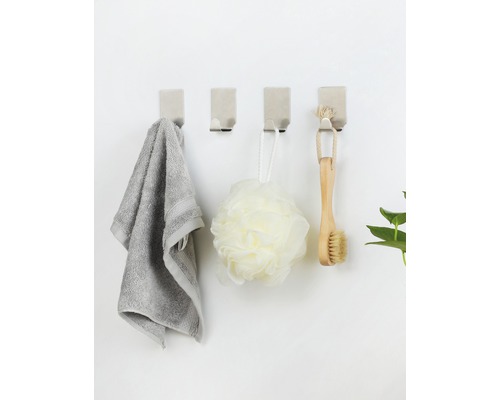 Fyra väggkrokar med handduk, badsvamp och borste på en vägg