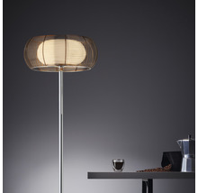 Golvlampa med metallskärm och sfärisk form bredvid ett bord med en kaffekopp och en mokabryggare