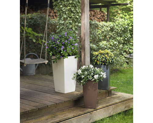 Tre höga planteringskärl med färgglada blommor på en träterrass