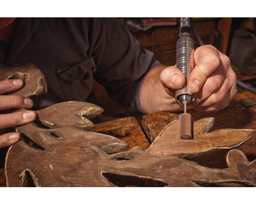 Hantverkare bearbetar träsnideri med roterande verktyg.