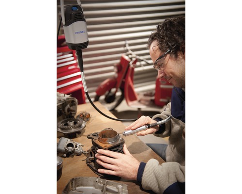 Man använder Dremel multiverktyg på ett motorblock på en arbetsbänk