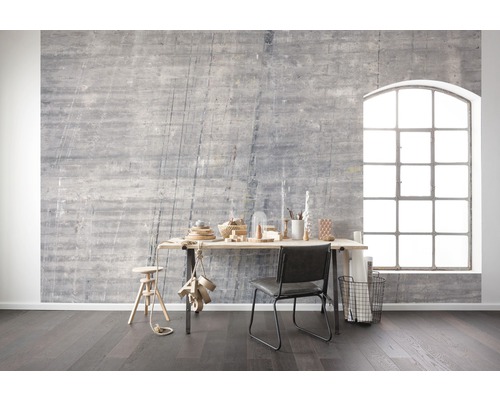 Vardagsrum med grå betongvägg, skrivbord, stol och stort fönster för en ljus och modern atmosfär.