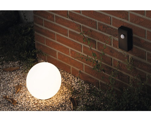 Miljöbild med en rund utomhuslampa och en rörelsesensor på en tegelvägg