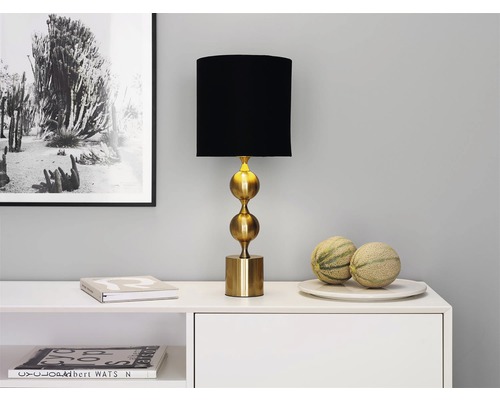 Dekorativ bordslampa med svart skärm och gyllene bas på en skänk