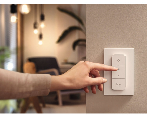 En hand använder en Philips Hue dimmer på väggen.