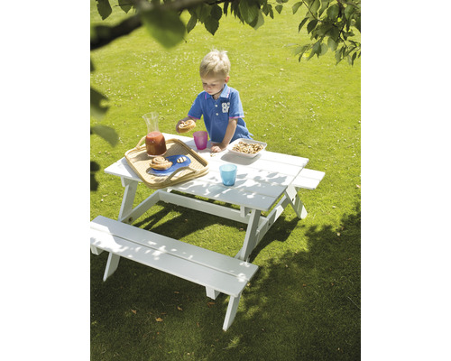 Trädgårdsscen med en pojke vid ett vitt picknickbord för barn med mat och dryck.