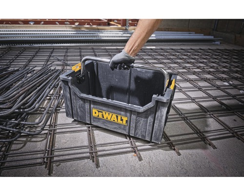 En person bär en verktygslåda av märket Dewalt på en byggarbetsplats.