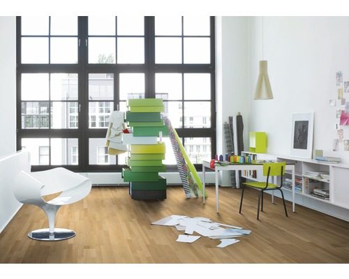 Ljust rum med trägolv, stort fönster, vit fåtölj, skrivbord och färgglada lådor