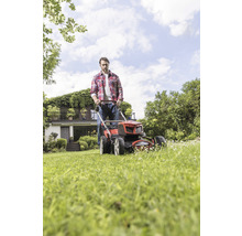 Man klipper gräsmattan med gräsklippare i trädgården framför huset.