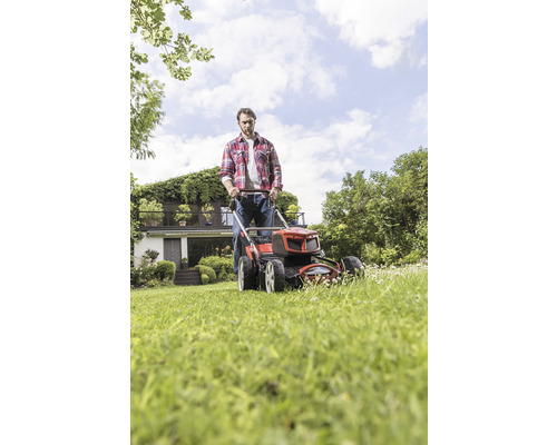 Man klipper gräsmattan med gräsklippare i trädgården framför huset.