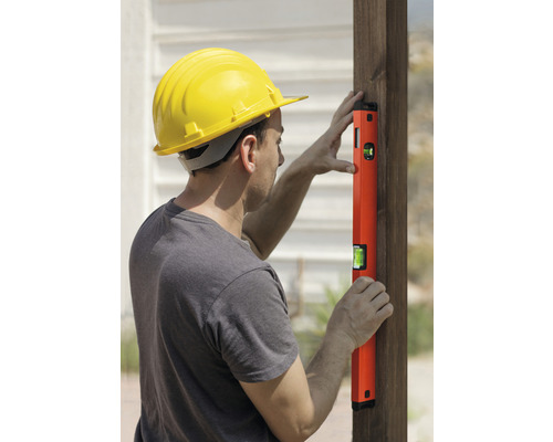 Man med skyddshjälm och vattenpass på en trästolpe