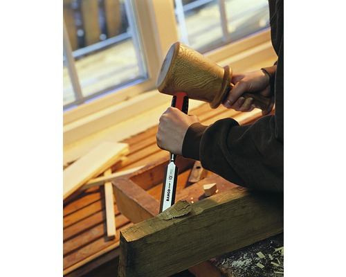 En person bearbetar en bit trä med en träklubba och ett stämjärn.