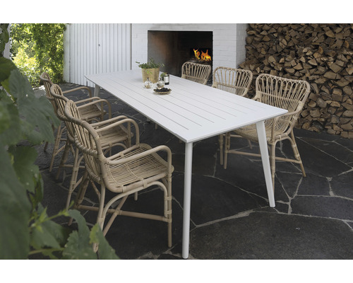 Matgrupp utomhus med vitt bord och rottingstolar framför en stapel ved