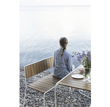 Kvinna sitter på en träbänk vid stranden bredvid ett bord med blommor.