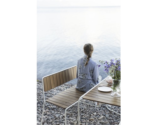 Kvinna sitter på en träbänk vid stranden bredvid ett bord med blommor.