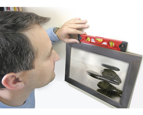 En person justerar en inramad bild med ett vattenpass.