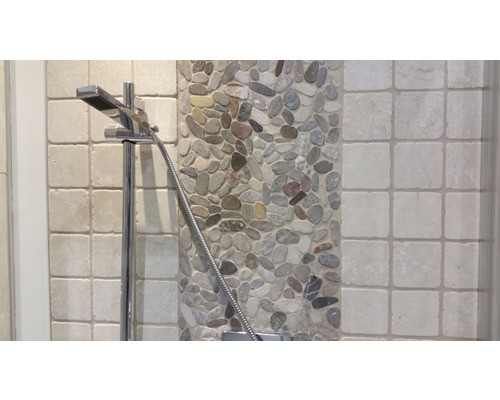 Detaljbild av ett duschhuvud mot en bakgrund av stenar och kakel