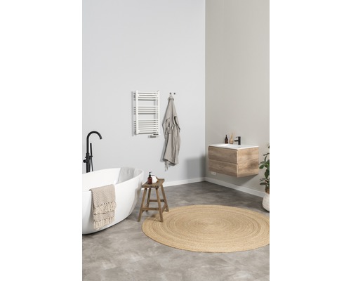 Ljust badrum med fristående badkar, underskåp för handfat, handdukstork och rund matta