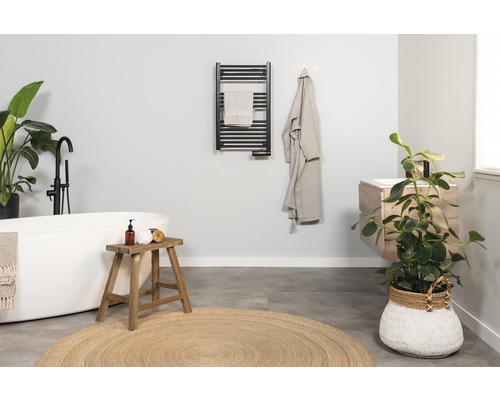 Ljust badrum med badkar, handfat, handdukstork och krukväxter för en vänlig atmosfär