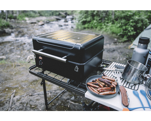 Bärbar grill med digital display och korvar på en tallrik utomhus.