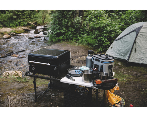 Campingplats med grill, tält och köksutrustning bredvid en bäck.