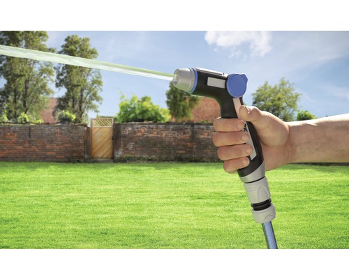 Hand som håller trädgårdsspruta med vattenstråle framför trädgårdsscen