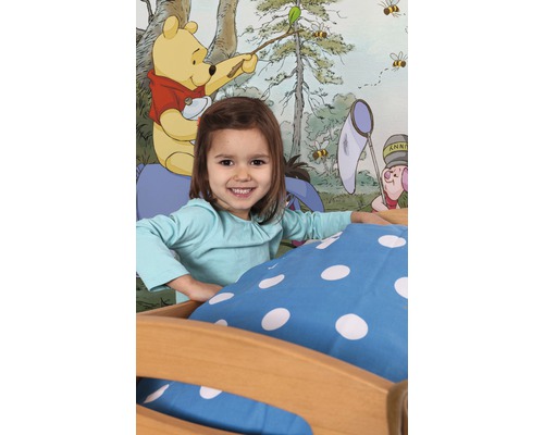 Flicka i sängen framför en tapet med Nalle Puh-motiv.